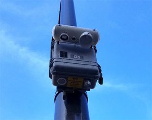 A photo of a plastic box attached to a pole, with an air monitoring device attached to the side.