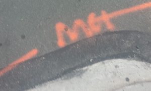 Orange spraypaint on an asphalt street, spelling "MCI"