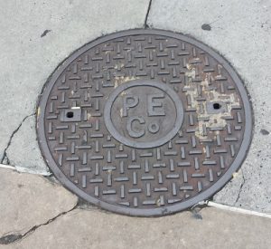 A manhole cover with letters in the center that spell "P E Co"
