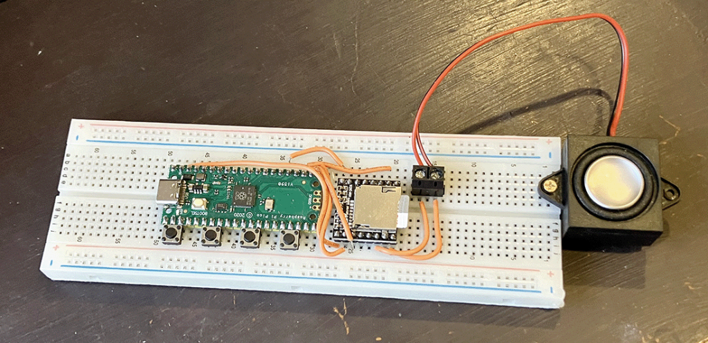 Photo of an assembled breadboard MP3 player, with two boards connected by orange wires and a speaker screwed into the end of the breadboard