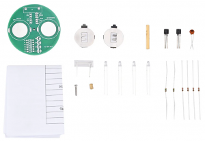 Photo of components for the LED Top Soldering Kit on a white background: round green circuit board, paper instructions, coin battery clips, LEDs, resistors, etc.