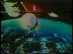 Old video still of a metal cylinder detaching from a spacecraft, with the earth's horizon in the background
