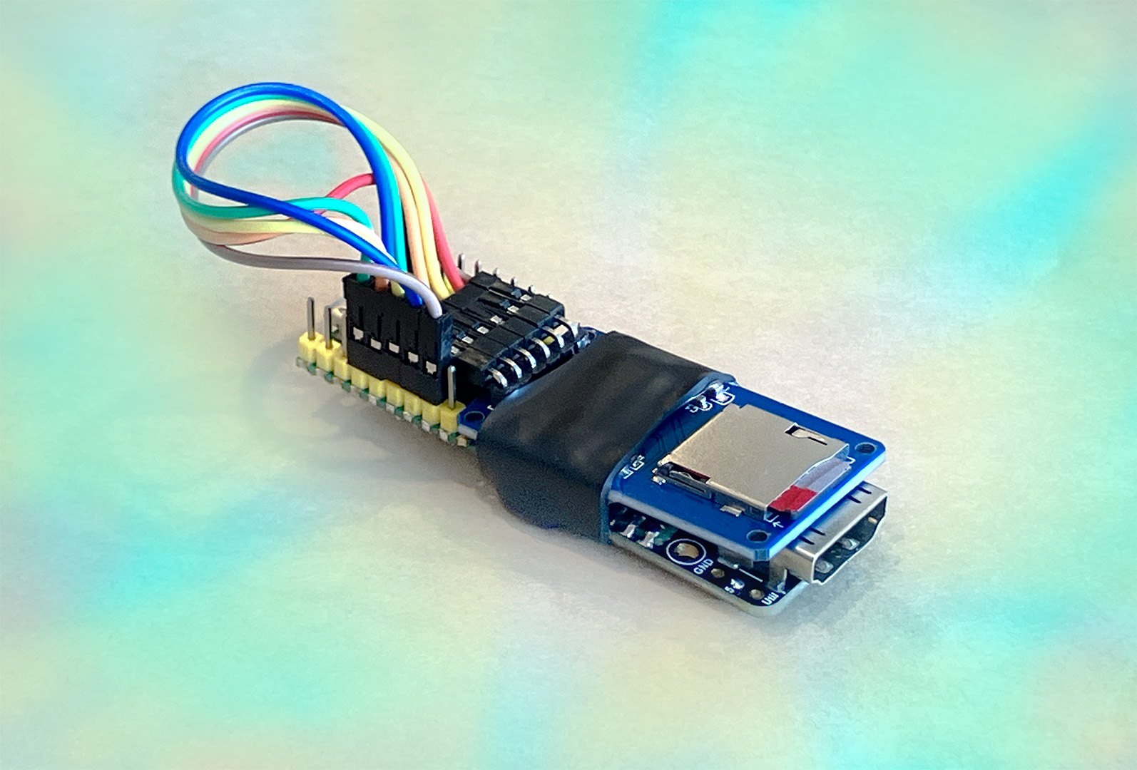 Photo of a DIY Digital Picture Frame device with tie-die colors in the background. The device is a Pi Pico microcontroller connected to a microSD card interface via 6 colorful wires