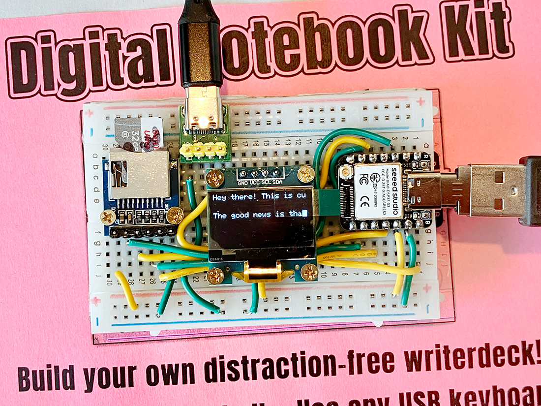 Photo of a Digital Notebook Kit from Iffy Books, with an ESP32-S3 microcontroller, a 1-inch OLED screen, and a microSD card reader on a breadeboard with green and yellow wires. A USB keyboard is connected on the right side, and the screen shows the first few words of the first two paragraphs of this post.