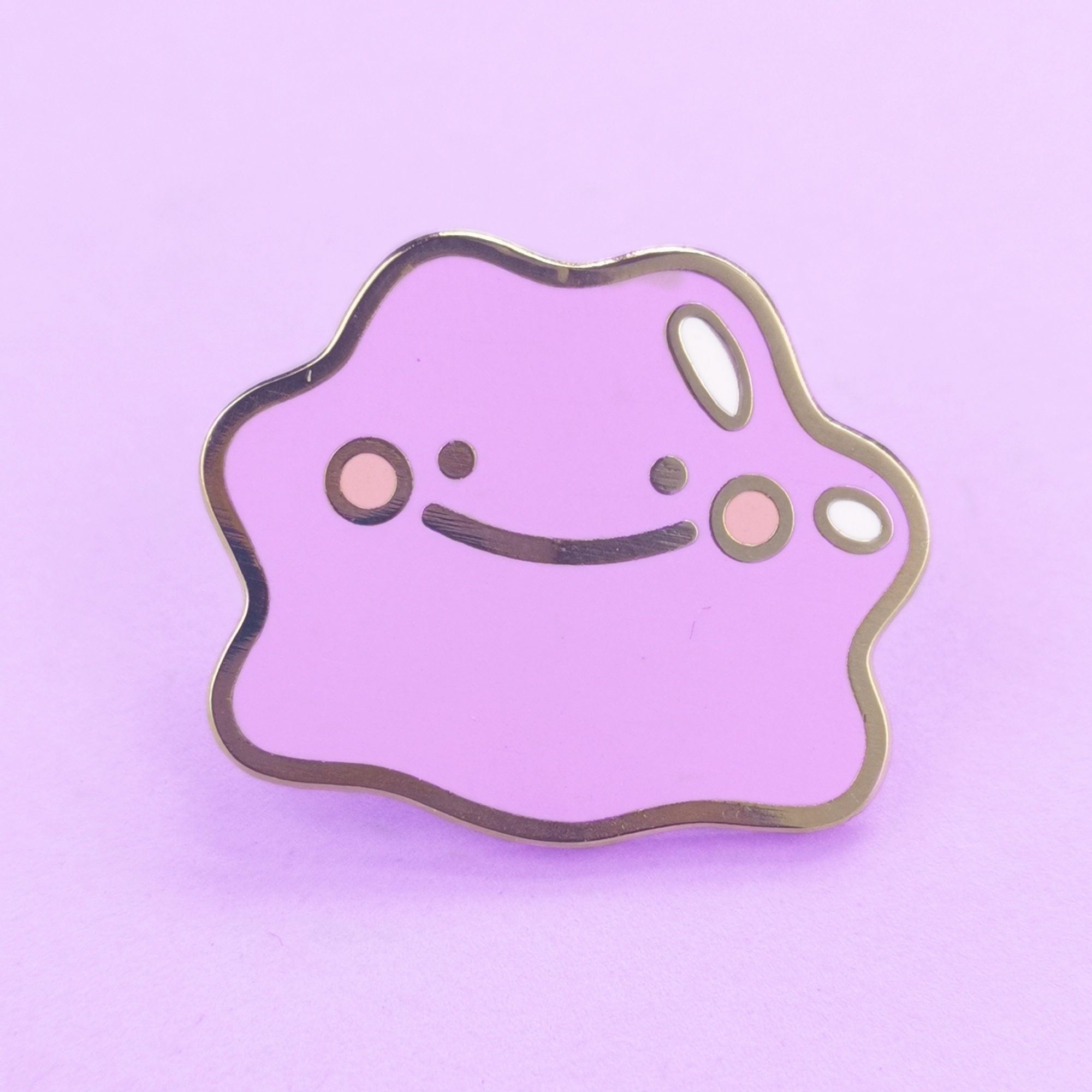 An enamel pin depicting a smiling purple blob that resembles Ditto, a Pokemon character.
