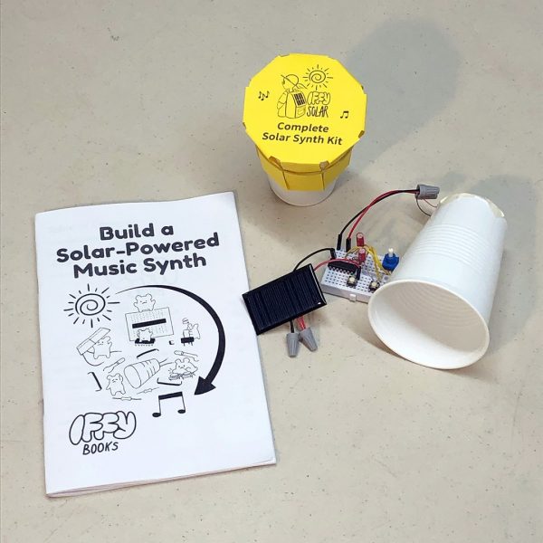 An assembled solar synthesizer kit on a white breadboard, with a small solar panel and a piezo speaker attached to a plastic cup. To the left is an unopened kit in a plastic cup, with a yellow paper label on top that says "Complete Solar Synth Kit." On the far left is a zine titled "Build a Solar-Powered Music Synth," with an illustration of hamsters assembling a circuit under a spiral sun and a curving arrow pointing to two music notes. The Iffy Books logo is in the bottom left.