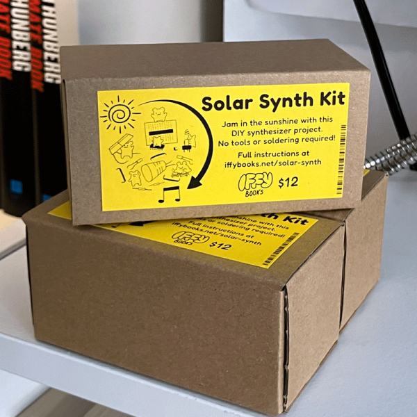 A stack of three solar synth kits at Iffy Books. The box brown cardboard, 4 inches by 2 inches by 2 inches, with a yellow label glued to the top. There's a drawing of cute hamsters assembling electronic parts in the sunshine, with the following text: Solar Synth Kit Jam in the sunshine with this DIY synthesizer project. No tools or soldering required. Full instructions at iffybooks.net/solar-synth Iffy Books $12