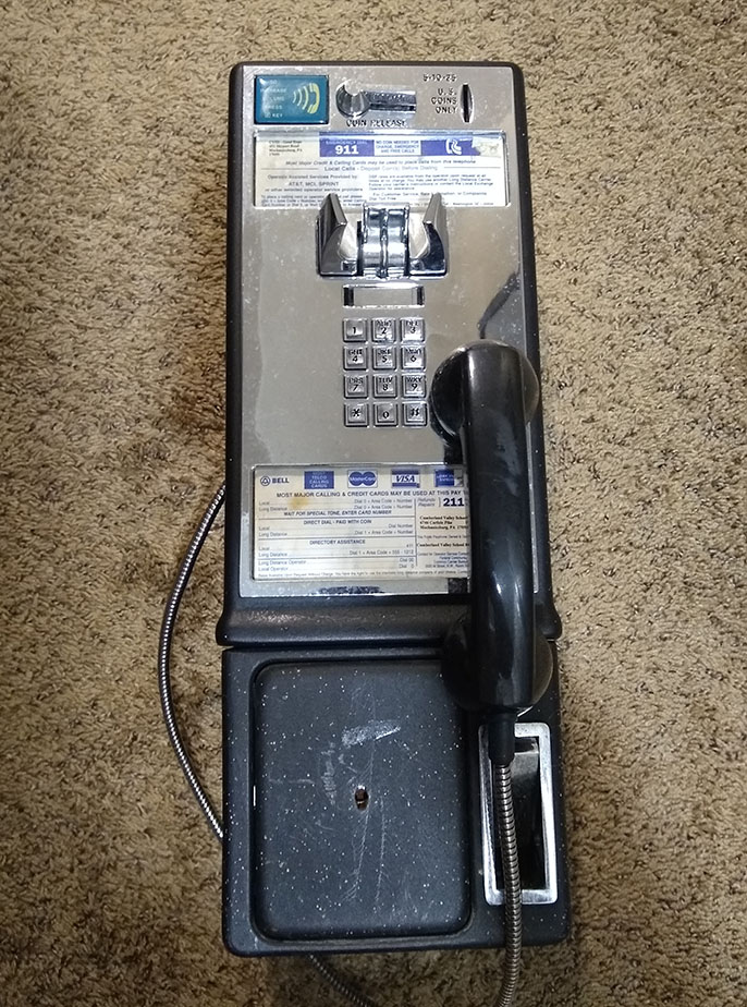 Photo of a Bell-era payphone with a chrome faceplate lying on a beige carpet.