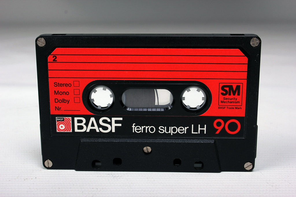 A photo of an audio cassette tape, made of black plastic with a red label. The brand is BASF, and the text says "ferro super LH 90"
