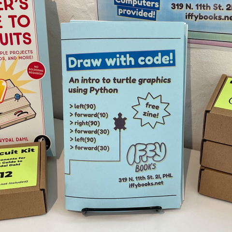 Closeup photo of a zine with the title "Draw with code! An intro to turtle graphics using Python." There's a turtle icon on the middle of the cover with a zig-zagging line coming out of its tail, and several lines of code on the left, such as "left(90)" and "forward(10)." Text on the right says "free zine!" The Iffy Books logo and address (319 N. 11th St. 2I, PHL) are at the bottom right corner.