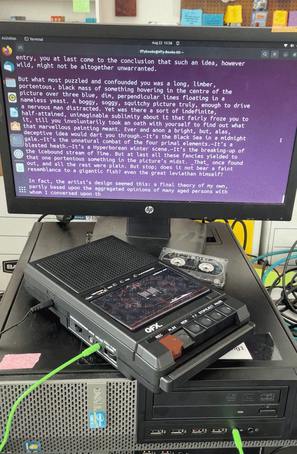 Photo of an audio cassette player attached to a computer, with the play button pressed down. Onscreen is an excerpt from Moby Dick, with a paragraph beginning, "But what most puzzled and confounded you was a long, limber, portentous, black mass of something hovering in the centre of the picture of three blue, dim, perpendicular lines floating in a nameless yeast."