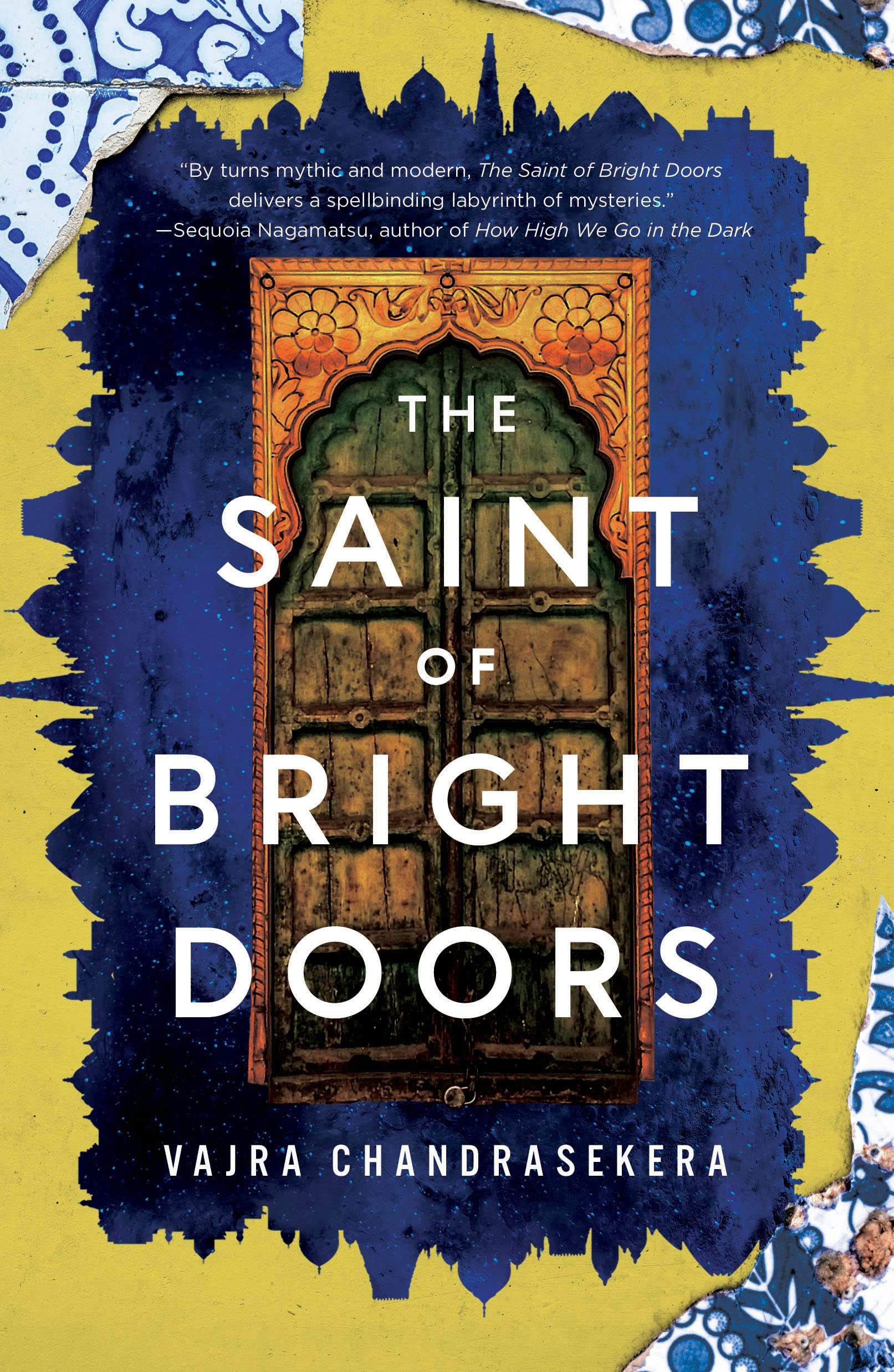 The cover of 'The Saint of Bright Doors' by Vajra Chandrasekera, with a pair of ornate doors surrounded by blue with yellow in the background, and pieces of broken chine scattered around the corners