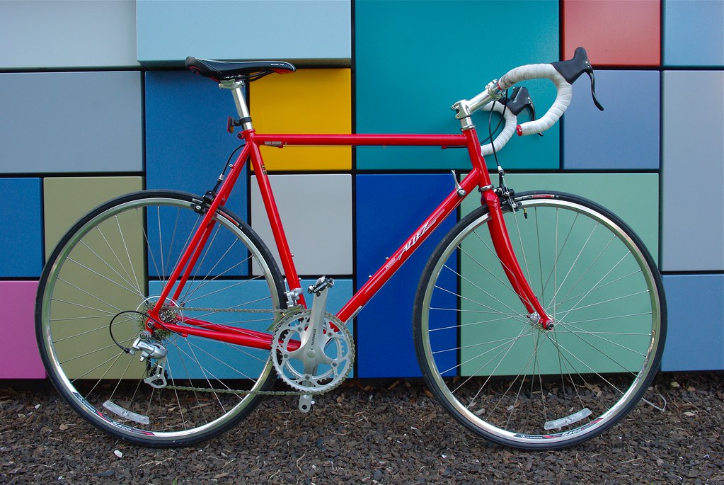 Photo of a red road bike in front of a building with colorful rectangular tiles