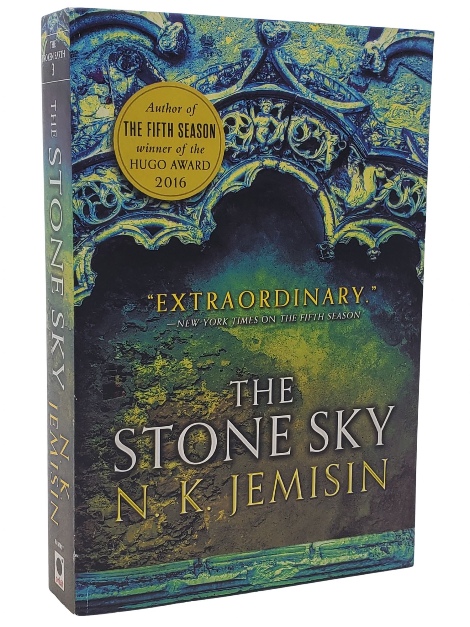 The front cover of 'The Stone Sky' by N. K. Jemisin, with a green-blue photo of intricate stone carving in the background