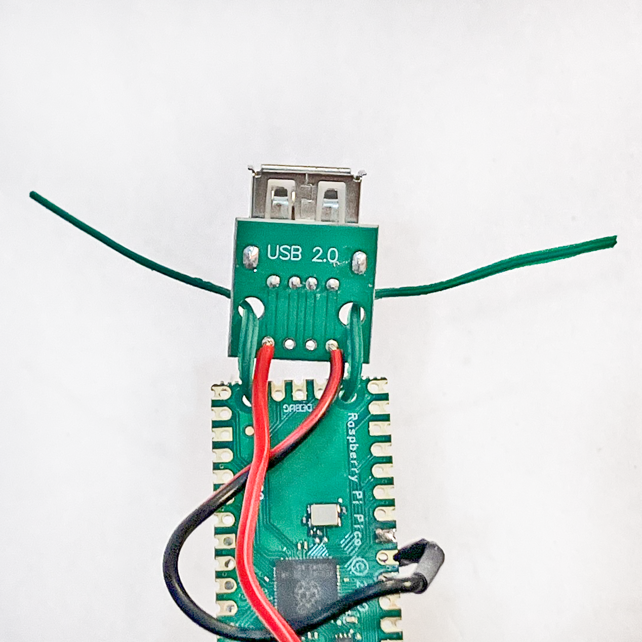 Pi Pico Development board with red and black wires running to a USB port, attached to the Pico with twist tie wire